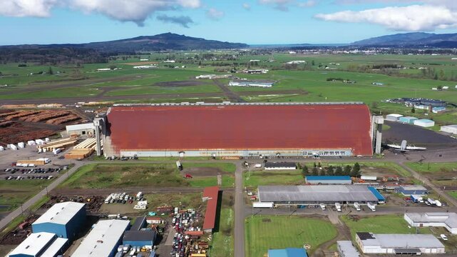 4K Drone aerial footage of Tillamook Air Museum building at Oregon Coast with a vintage airplane parked outside.  Green agricultural fields, travel, and tourism content