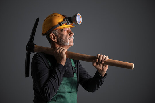 Mature miner man with pick axe on dark background