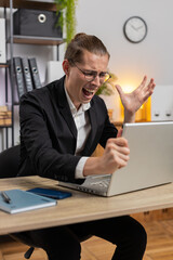 Sad young stylish businessman using laptop typing browsing, loses becoming surprised sudden lottery...