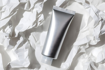 Realistic metallic cosmetic tube mockup placed on white crumpled paper background. Perfect for branding, packaging design, and skincare product presentation.