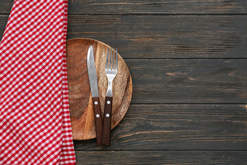 Table setting with plate, cutlery and checkered napkin on wooden background