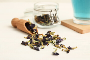 Wooden scoop with scattered butterfly pea flower tea and jar on white background, closeup