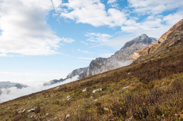 Grass-covered slopes in the Republic of Adygea with Fisht-Oshten massif in the background covered with morning fog, Russia
