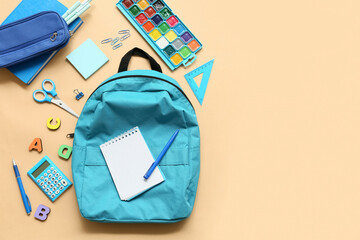 School backpack with different stationery supplies on beige background