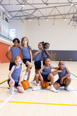 In school gym, group of diverse children posing with basketballs, smiling confidently © wavebreak3