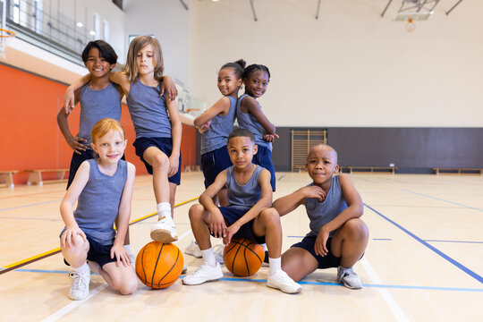 Group of school diverse children posing with basketballs in gym, smiling confidently