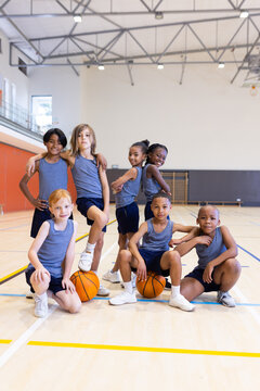 Fototapeta In school gym, group of diverse children posing with basketballs, smiling confidently