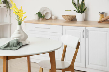 Vase with mimosa flowers on dining table in light kitchen