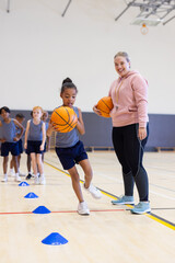 Playing basketball, girl dribbling ball in school gym with female coach smiling