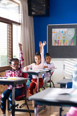 In school, diverse children raising hands in classroom, participating in lesson © WavebreakMediaMicro