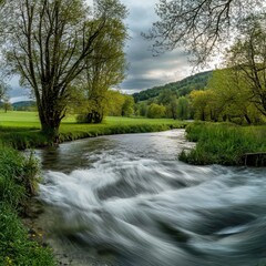 Obraz premium Serene River Flowing Through Lush Green Meadow Under Cloudy Sky