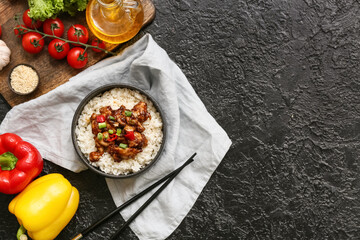 Tasty sweet and sour chicken with rice in bowl, vegetables and chopsticks on black grunge background