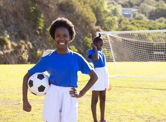 Obraz premium Smiling african american girl holding soccer ball on school field, teammate in background