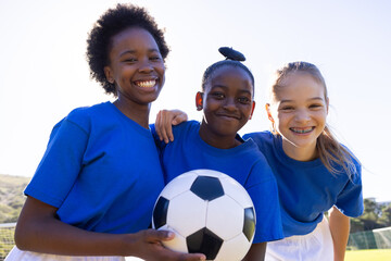 Smiling school diverse girls holding soccer ball, enjoying outdoor sports activity together