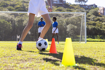 Naklejka premium Playing soccer, diverse girls practicing dribbling around cones on school field