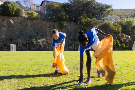 Picking up trash, diverse girls in school uniforms cleaning up field together