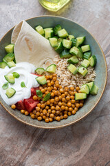 Plate with roasted chickpeas, brown rice, greek yogurt and vegetables, vertical shot on a brown granite background, high angle view