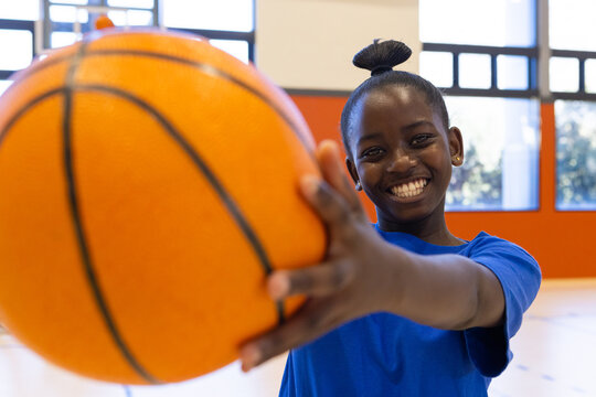 Smiling african american girl holding basketball in school gym, ready for practice - Powered by Adobe