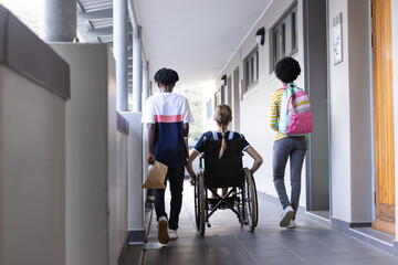Walking in school hallway, diverse students with backpacks and wheelchair, heading to class