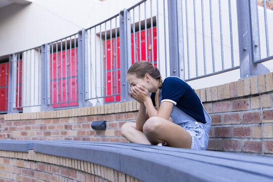 Sitting alone, girl crying with hands covering face at school