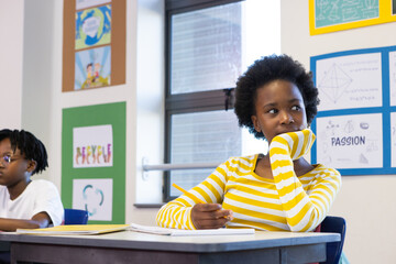 In school, african american girl in striped shirt daydreaming while holding pencil in classroom