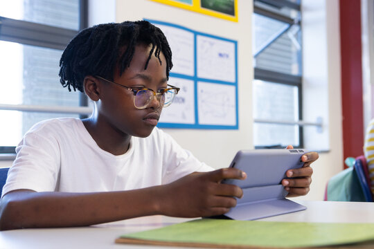 In school, african american boy using tablet at desk, focusing on digital learning