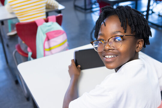 In school, african american boy using tablet and smiling while sitting at desk