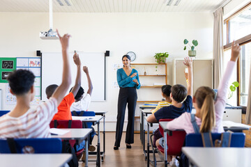 Indian female teacher in classroom, students raising hands to answer question in school