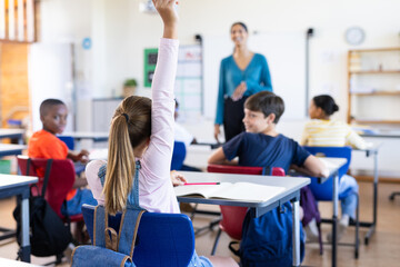 In school, student raising hand to answer question in classroom with Indian female teacher