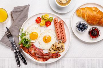 A classic breakfast plate featuring sunny-side-up eggs, crispy bacon, sausages, and fresh tomatoes