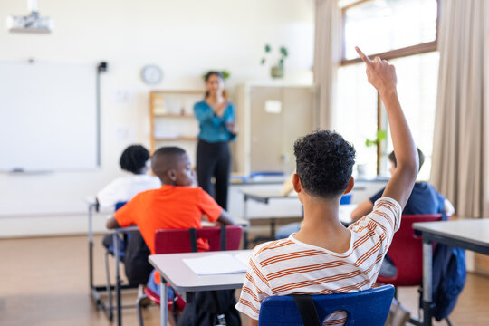In school, student raising hand to ask question in classroom with Indian female teacher