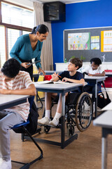 In school, Indian female teacher assisting student in wheelchair during classroom activity