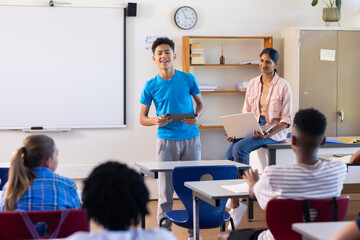 Presenting project in school, boy holding tablet while Indian female teacher and students watching
