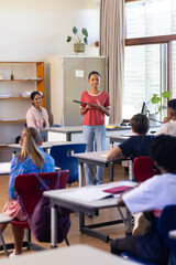 Holding book, woman teaching in classroom with students listening attentively in school