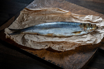 Fresh raw whole fish herring on parchment paper on wooden cutting board, top view, closeup