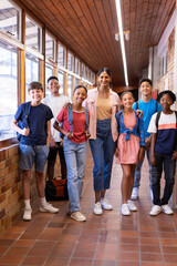 Obraz premium Indian female teacher standing with group of students in school hallway, all smiling