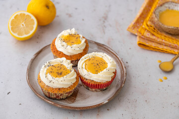 Lemon Poppy Seed Cupcakes with lemon curd and cream cheese topping. Cupcake in form of Fried Egg. Colourful Easter eggs, flowers on a stone background. Spring concept. Easter holiday and festive food.