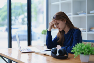 Stressed young woman overwhelmed by e-learning studies at desk with laptop, notebook, headphones,...