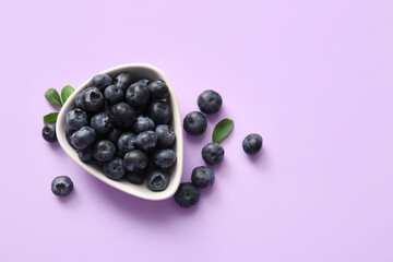 Bowl of fresh ripe blueberry on lilac background, closeup