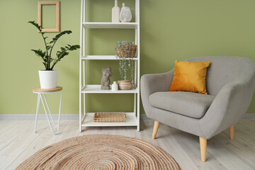Interior of modern room with comfortable armchair and shelving unit near green wall