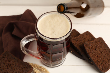 Mug of fresh kvass with slices of bread and wheat on white wooden background