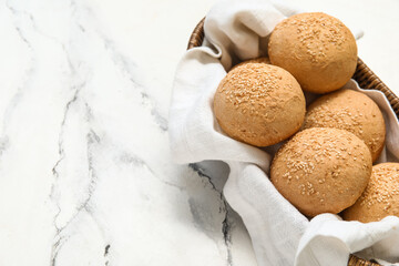 Wicker bowl of fresh buns with sesame seeds on white background