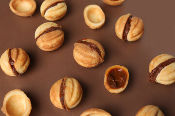 Many sweet walnut shaped cookies with boiled condensed milk on brown background