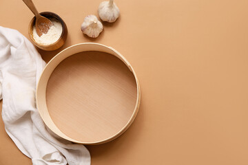 Wooden sieve, bowl of flour, garlic and napkin on color background