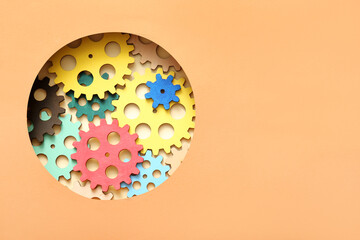 Wooden gears visible through round hole in orange paper