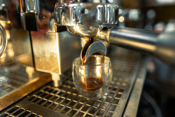 A shot of coffee flows into a glass from a coffee machine in a coffee shop.