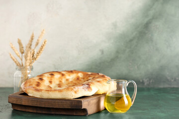 Wooden tray with tasty lavash and jug of oil on green grunge table