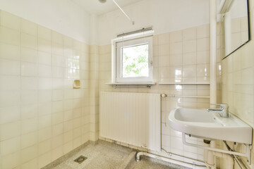 A spacious and bright bathroom showcasing a clean design with tiled walls, a basin, and a window allowing natural light to flow in.