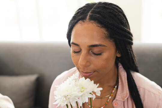 Woman enjoying fresh white flowers at home, eyes closed in peaceful moment