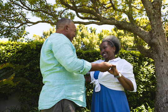 Dancing joyfully in garden, senior couple under large tree enjoying time together